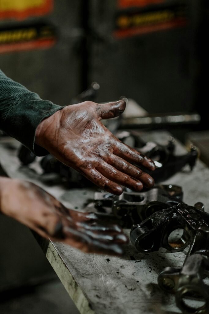 Close-up of a mechanic's hands covered in grease while working on engine parts in a workshop.