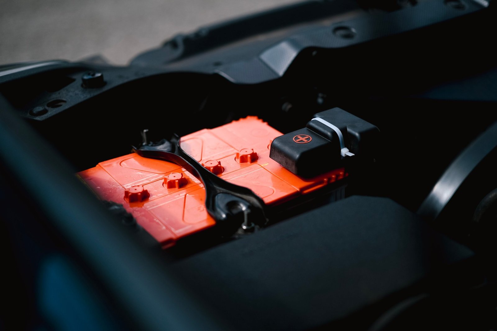 electric-vehicle-service-in-dubai.Detailed view of an orange car battery inside a vehicle's engine bay, highlighting its features.