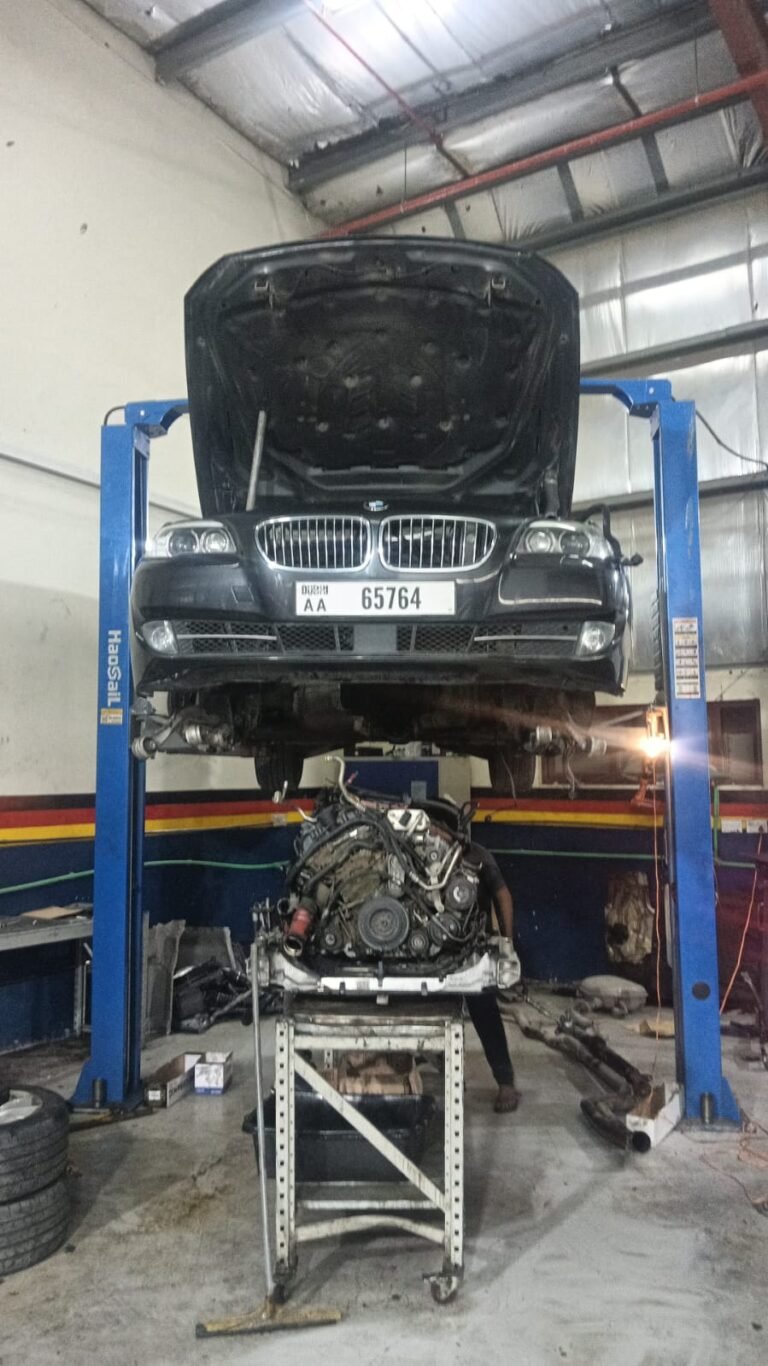 BMW on a workshop lift with an engine assembly positioned beneath the vehicle.